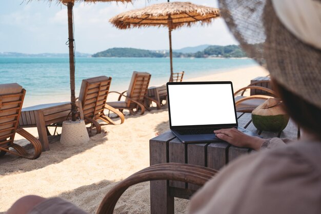 Imagen de una mujer que usa y toca el panel táctil de una computadora portátil con una pantalla de escritorio en blanco mientras está sentada en la playa