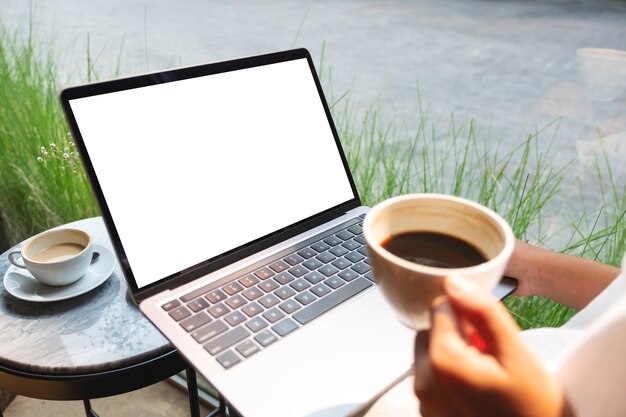 Imagen de una mujer que usa y trabaja en una computadora portátil con una pantalla de escritorio blanca en blanco mientras bebe café en un café