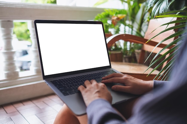 Imagen de una mujer que usa y trabaja en una computadora portátil con una pantalla de escritorio blanca en blanco mientras se sienta en el balcón de su casa