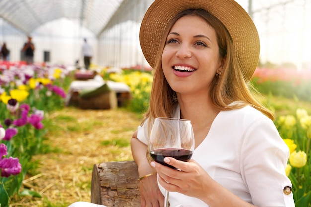 Imagen de una mujer riendo y brillante sentada entre flores en el bar al aire libre del jardín sosteniendo una copa de vino en primavera