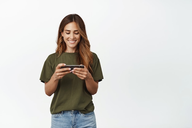 Foto imagen de mujer sonriente jugando videojuegos, viendo videos en línea con celular 4g en internet en un teléfono inteligente