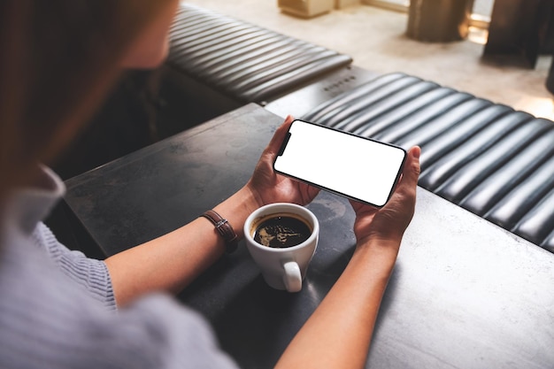 Imagen de una mujer sosteniendo un teléfono móvil con una pantalla de escritorio blanca en blanco con una taza de café sobre la mesa