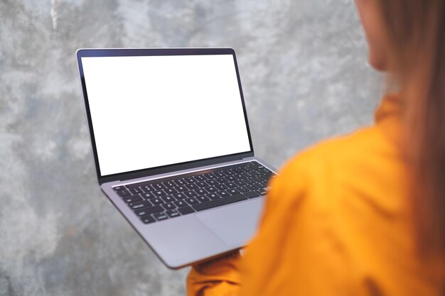 Imagen de una mujer sosteniendo y usando una computadora portátil con una pantalla de escritorio blanca en blanco al aire libre