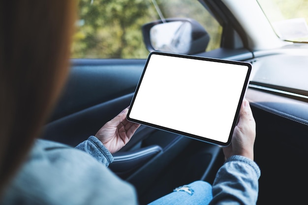 Imagen de una mujer sosteniendo y usando una tableta digital con pantalla en blanco en el auto