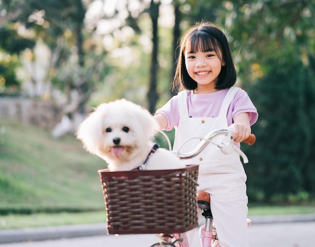 Imagen de una niña asiática en bicicleta con su perro mascota en el parque