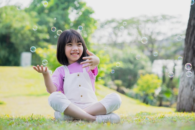 Imagen de una niña asiática jugando con pompas de jabón en el parque