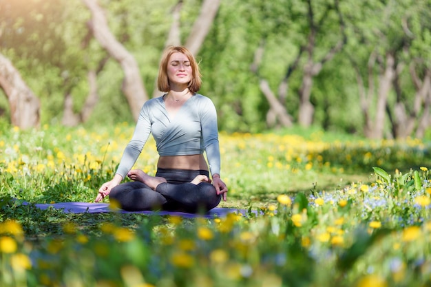 Imagen de niña haciendo yoga sentada en posición de loto sobre una alfombra azul en el bosque en verano