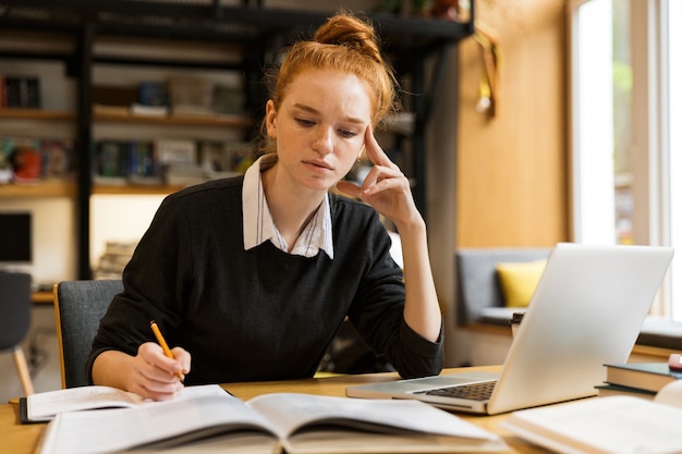 Imagen de niña inteligente estudiando, mientras está sentado en el escritorio en la biblioteca de la universidad con pared de estantería