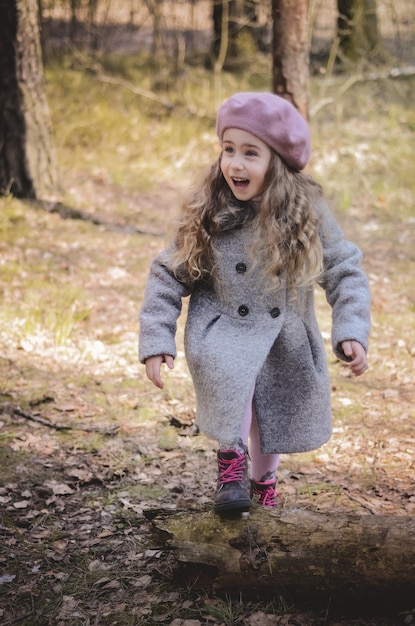 Imagen de una niña de pelo largo de estilo antiguo con una boina y un abrigo caminando por el bosque