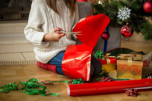 Imagen de niña sentada bajo el árbol de Navidad y cortar papel de regalo