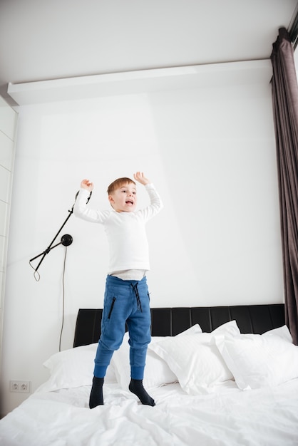 Imagen de niño feliz saltando en la cama en casa. Mira a un lado.