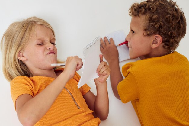 Imagen de niño y niña positivos dibujando en cuadernos tirados en el suelo con fondo claro inalterado