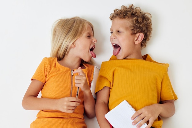 imagen de un niño y una niña positivos yacen en el suelo con blocs de notas y lápices aislados de fondo sin alterar. foto de alta calidad