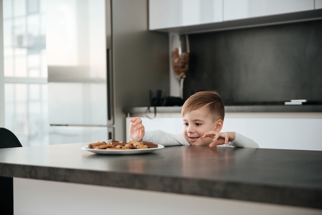 Imagen de niño de pie en la cocina mientras intenta tomar galletas y chocolate.