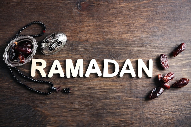 Imagen de la palabra RAMADAN con rosario y dátiles de frutas sobre fondo de madera de cerca