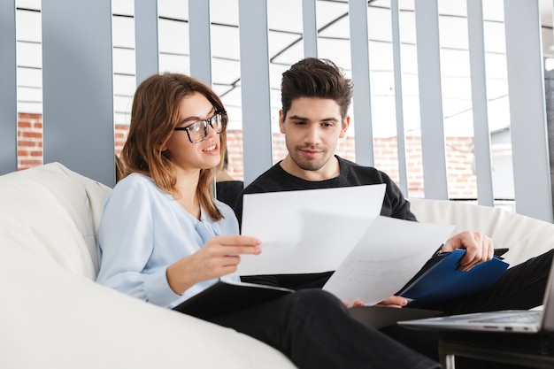 Imagen de una pareja amorosa joven concentrada en casa en el interior usando la computadora portátil trabajar con documentos.