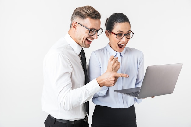 Imagen de la pareja joven de colegas de negocios aislada sobre la pared blanca usando la computadora portátil hace gesto del ganador.