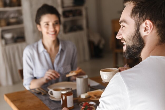 Imagen de pareja morena positiva hombre y mujer comiendo juntos en la mesa mientras desayuna en el apartamento