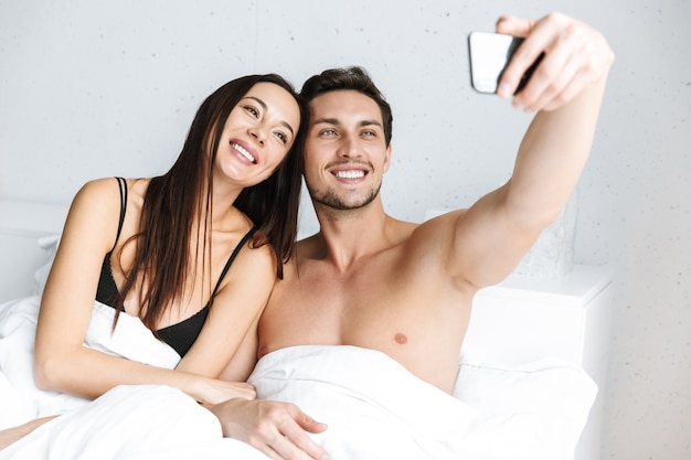 Imagen de pareja romántica tomando selfie en teléfono celular, mientras está acostado en la cama en casa o apartamento de hotel