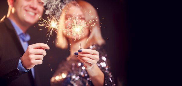 Imagen de pareja sonriente con luces de Bengala sobre fondo negro