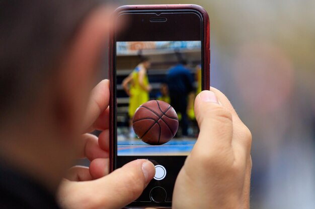 Foto la imagen de la pelota de baloncesto aparece en el teléfono inteligente de la tableta en las manos del hombre fondo borroso