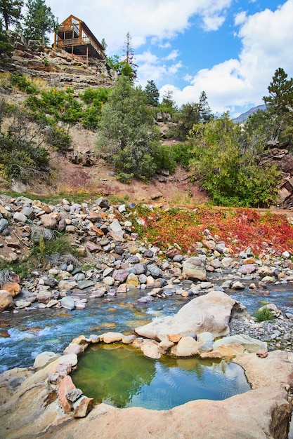 Imagen de una pequeña fuente termal natural junto al río y los acantilados con cabaña en la parte superior