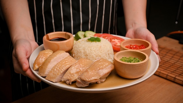 Imagen de un plato de cocina asiática Una camarera sirve arroz con pollo de Hainan con salsa de chile