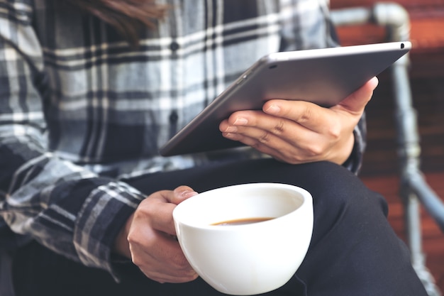 Imagen del primer de una mujer que sostiene y que usa la PC de la tableta mientras que bebe el café en café