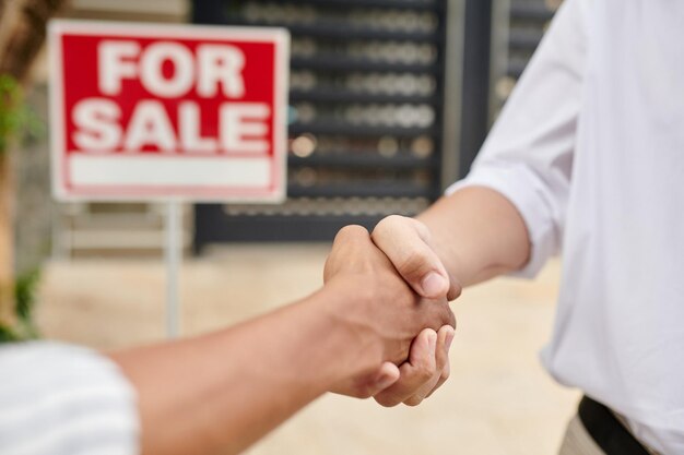 Imagen de primer plano de un agente de bienes raíces saludando a un cliente frente a una casa en venta