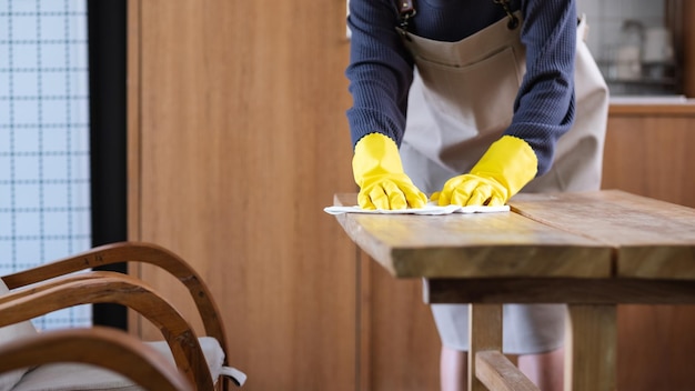 Foto imagen de primer plano de un ama de casa con guantes protectores limpiando y lavando la mesa de madera en casa