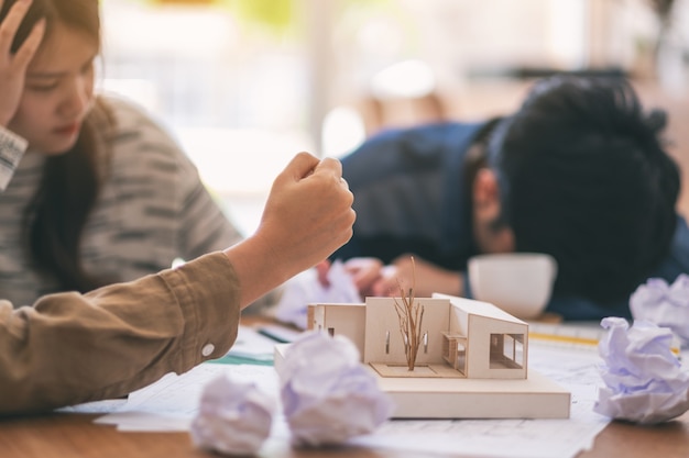 Imagen de primer plano de arquitectos enojados y estresados intentan destruir un modelo de arquitectura en la mesa con la mano cuando fallan en el trabajo