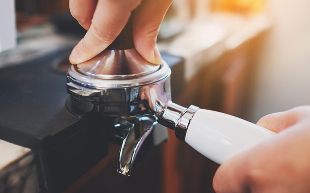 Imagen de primer plano de un barista usando un manipulador para presionar el café molido en un portafiltro en una cafetería