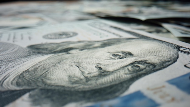Imagen en primer plano de Benjamin Franklin en un montón de billetes de cien dólares estadounidenses