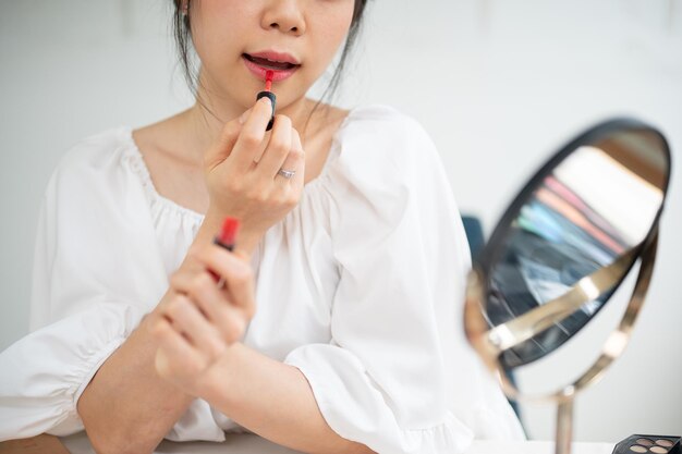 Imagen en primer plano de una bonita mujer asiática aplicando lápiz labial en sus labios haciendo su maquillaje diario