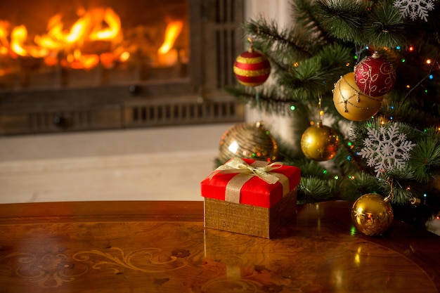 Imagen de primer plano de la caja de regalo roja sobre la mesa de madera delante de la chimenea y el árbol de Navidad. Lugar vacío para texto