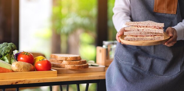 Imagen de primer plano de una chef cocinando y sosteniendo un plato de sándwich de queso de jamón de trigo integral en la cocina