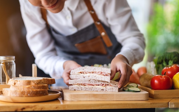 Imagen de primer plano de una chef cocinando y sosteniendo un trozo de sándwich de queso de jamón de trigo integral en la cocina