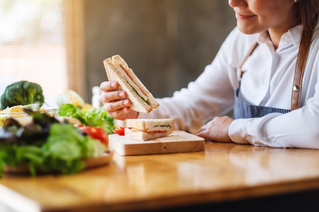 Imagen de primer plano de una cocinera cocinando y comiendo un sándwich de trigo integral en la cocina