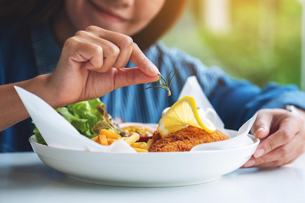 Imagen de primer plano de una cocinera cocinando y decorando un plato de pescado y patatas fritas