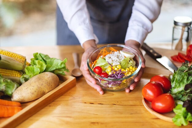 Imagen de primer plano de una cocinera cocinando y sosteniendo un plato de ensalada de verduras mixtas frescas en la cocina