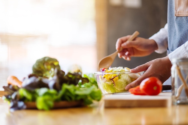 Imagen de primer plano de una cocinera cocinando y sosteniendo un plato de ensalada de verduras mixtas frescas en la cocina