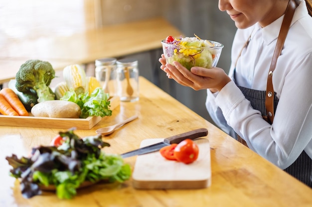 Imagen de primer plano de una cocinera cocinando y sosteniendo un plato de ensalada de verduras mixtas frescas en la cocina