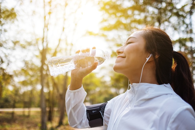 Imagen de primer plano de una corredora asiática bebiendo agua de botella después de trotar en el parque de la ciudad