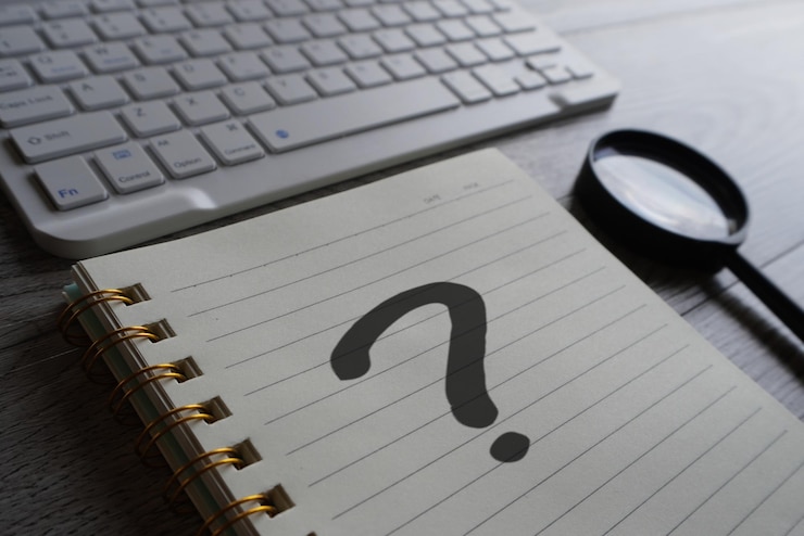 Foto imagen en primer plano de un cuaderno con lupa y teclado con signo de interrogación