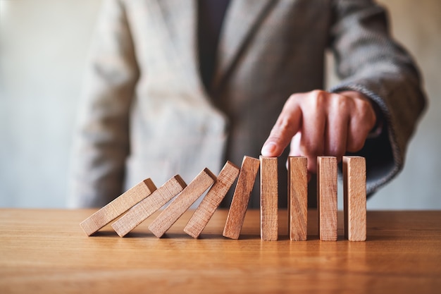 Imagen de primer plano del dedo de una empresaria intenta detener la caída de bloques de dominó de madera para el concepto de solución empresarial