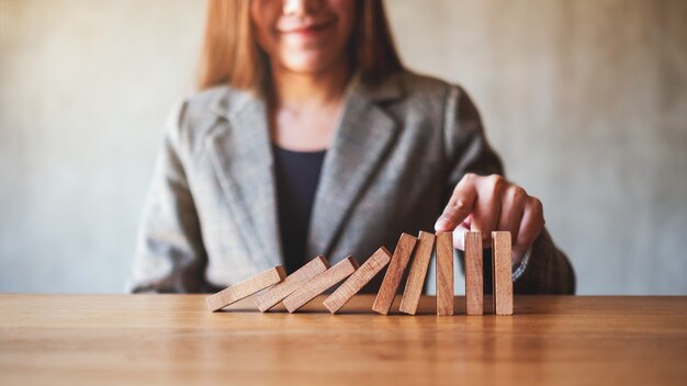 Foto imagen de primer plano de una empresaria intenta usar el dedo para detener la caída de bloques de dominó de madera para el concepto de solución empresarial