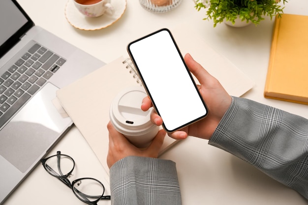 Imagen de primer plano Empresaria sosteniendo una taza de café y usando un teléfono inteligente sobre el escritorio de la oficina