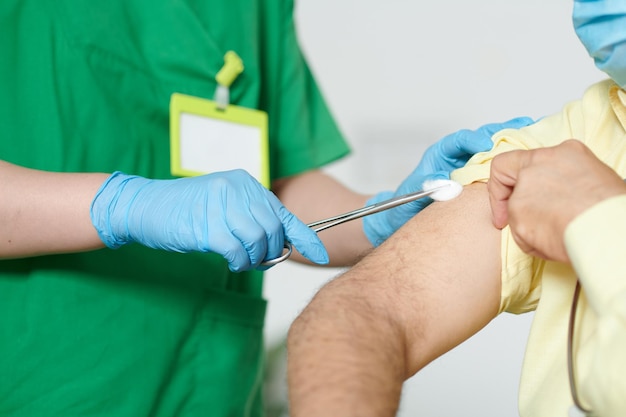 Imagen de primer plano de una enfermera con guantes de goma limpiando el hombro del paciente con una bola de algodón antes de inyectar la vacuna