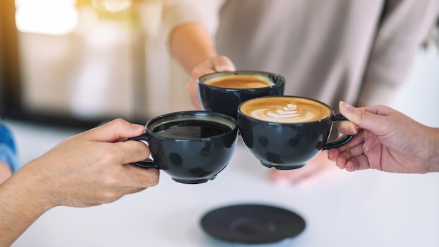 Imagen de primer plano de la gente disfrutaba bebiendo y tintineando tazas de café sobre la mesa en el café