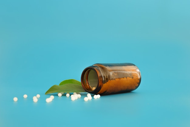 Imagen de primer plano de glóbulos homeopáticos en botella de vidrio sobre fondo azul. Farmacia de homeopatía, medicina herbal, natural, medicina homeopática alternativa, atención médica. Espacio libre, espacio de copia.